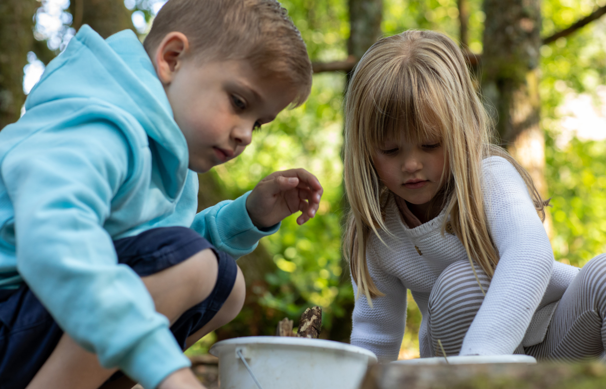 A young boy and girl collecting items in nature in buckets