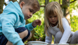 A young boy and girl collecting items in nature in buckets