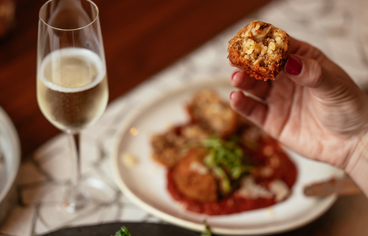 An arancini starter dish with a tomato sauce and a glass of prosecco