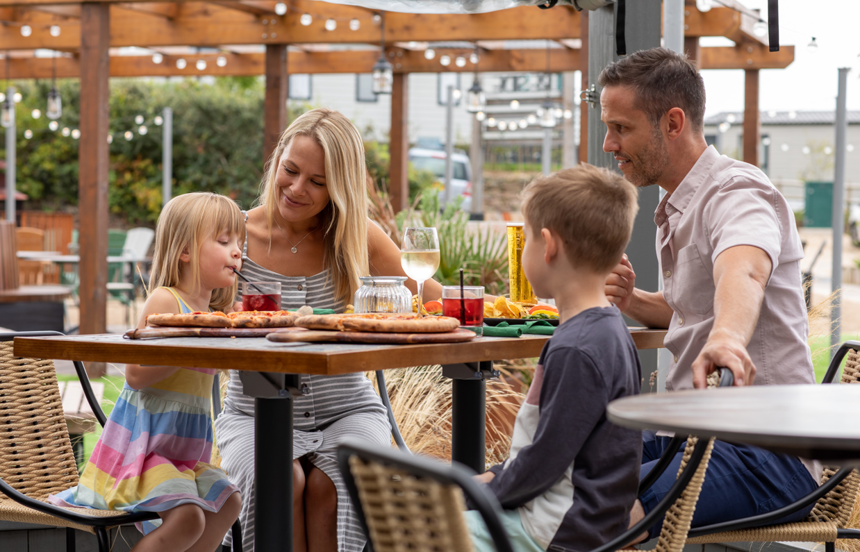 A family of four sat at a high outdoor table eating and drinking