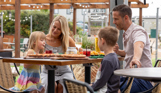 A family of four sat at a high outdoor table eating and drinking