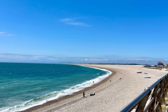 Chesil Cove Beach with striking blue water from the bottom of Portland with Weymouth in the distance