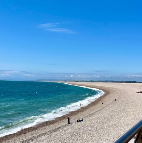 Chesil Cove Beach with striking blue water from the bottom of Portland with Weymouth in the distance