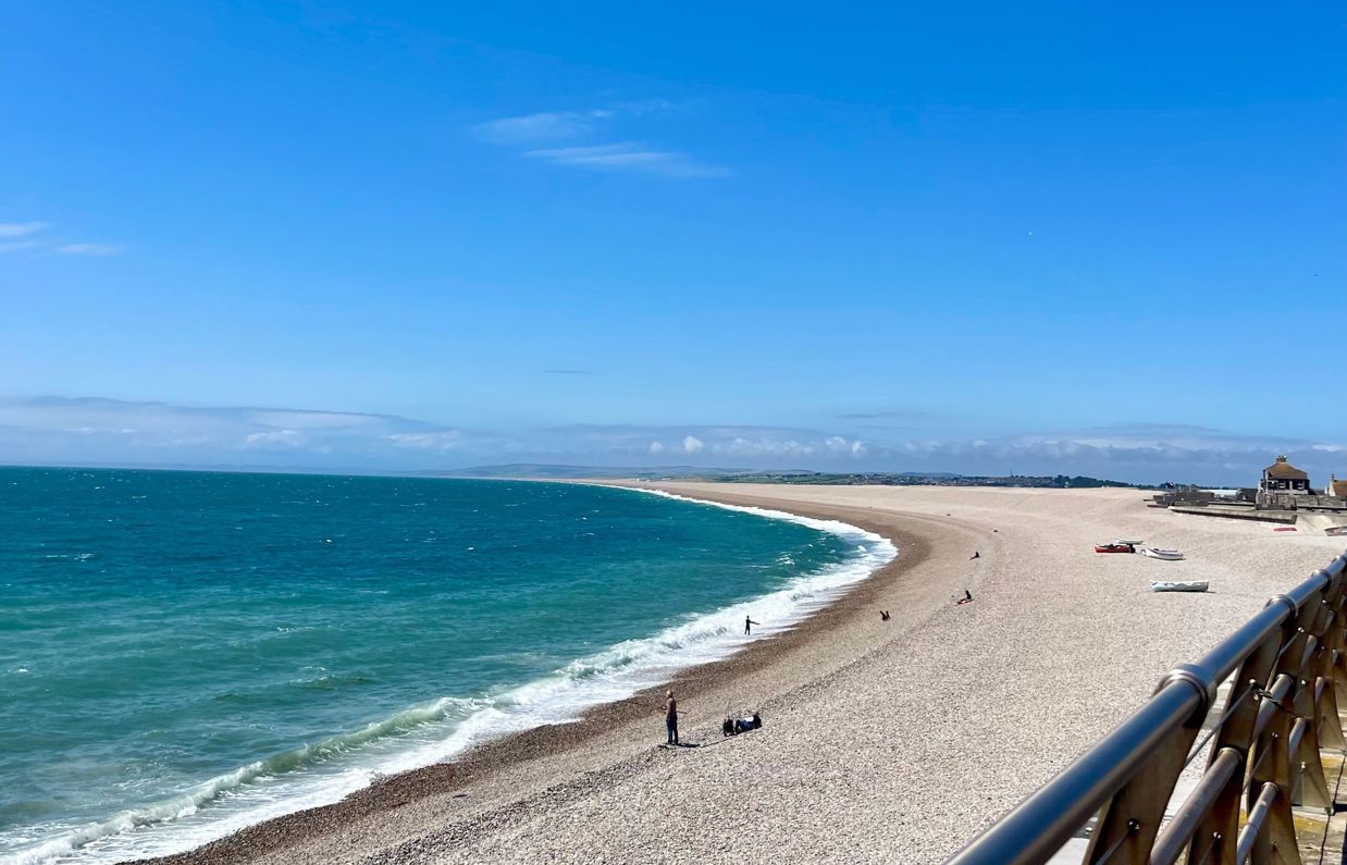 Chesil Cove Beach with striking blue water from the bottom of Portland with Weymouth in the distance