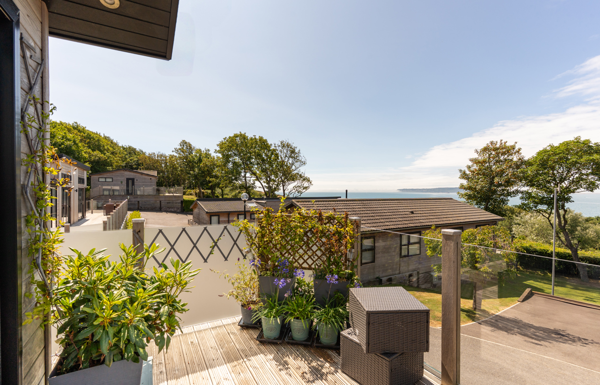The view of the sea and Weymouth from the Kingfisher area of Osmington Mills Lodge Park surrounded by lodges and trees on a sunny, blue sky day