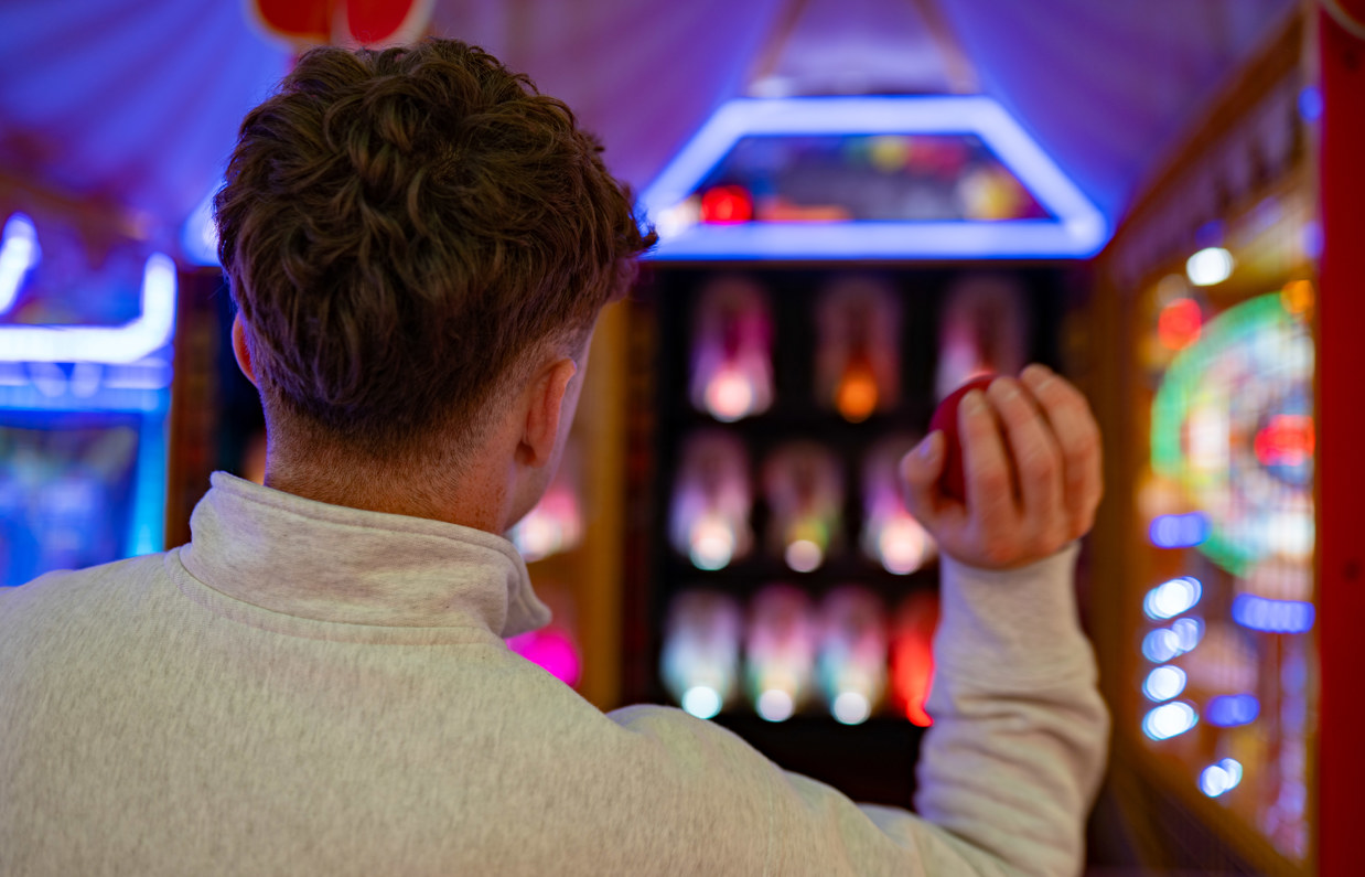 A young man throwing a ball at a Down the Clown arcade game