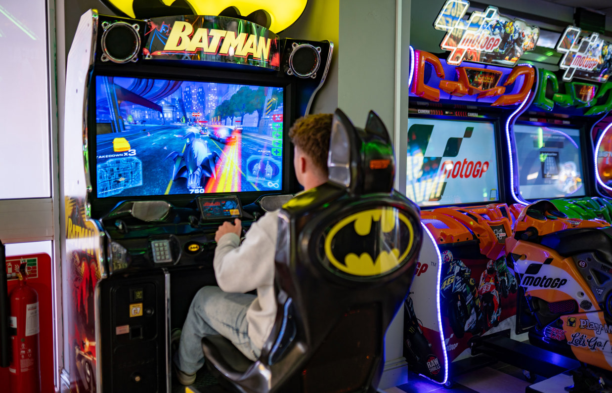 A young man sat playing a batman arcade game