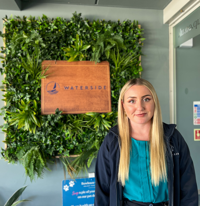 A smiling lady stood beside a Waterside sign