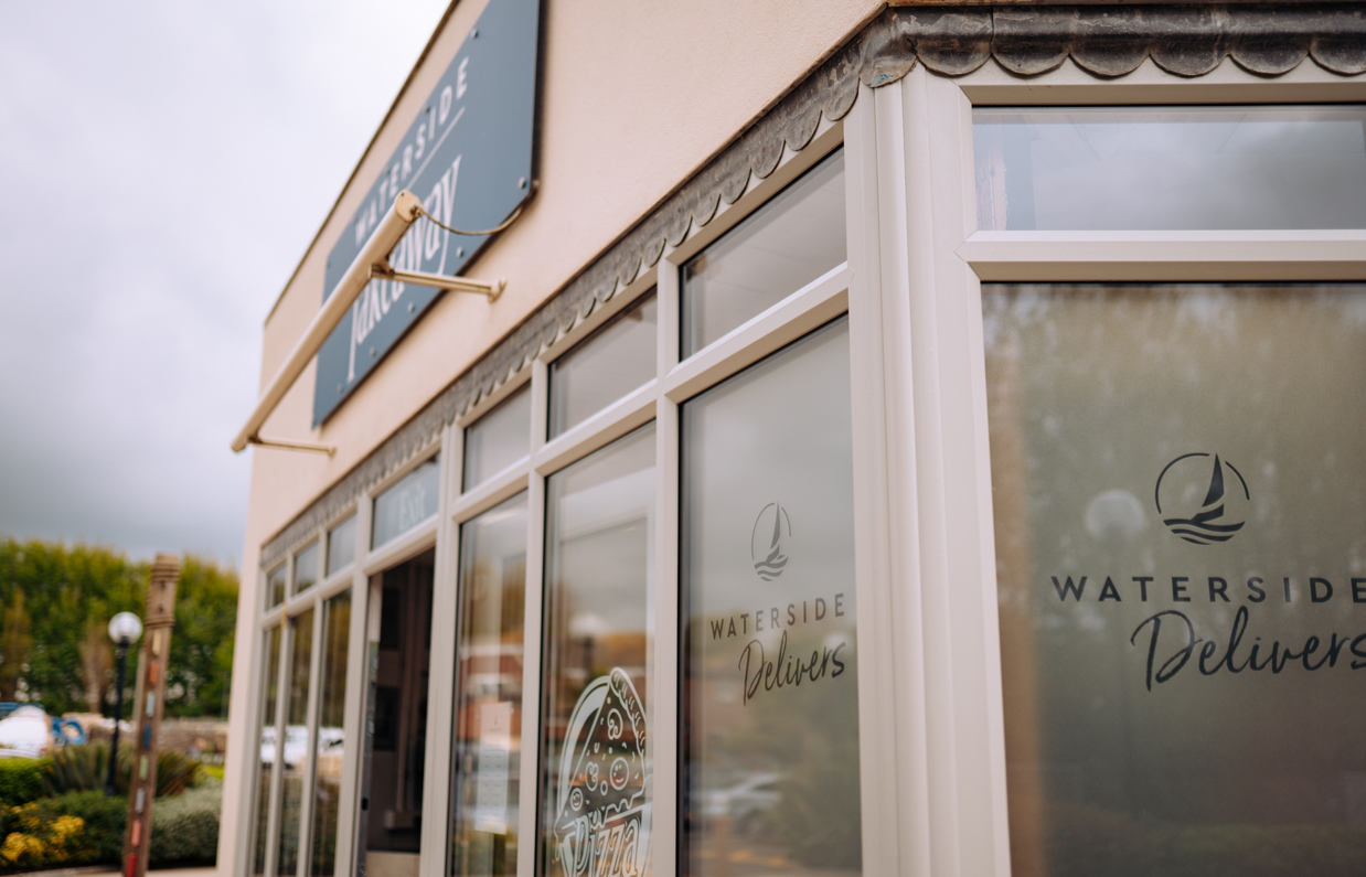 The outside of a fish and chip and pizza takeaway shop with 'Waterside Delivers' stickers on the windows