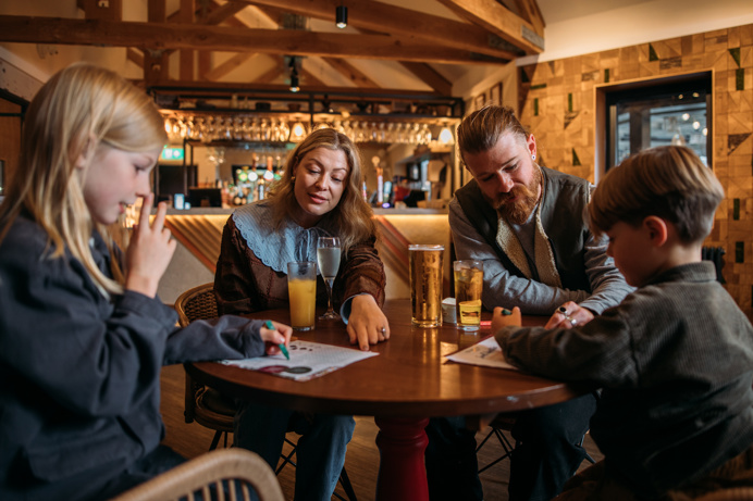 A couple sat with two young boys at an indoor table with drinks and colouring sheets