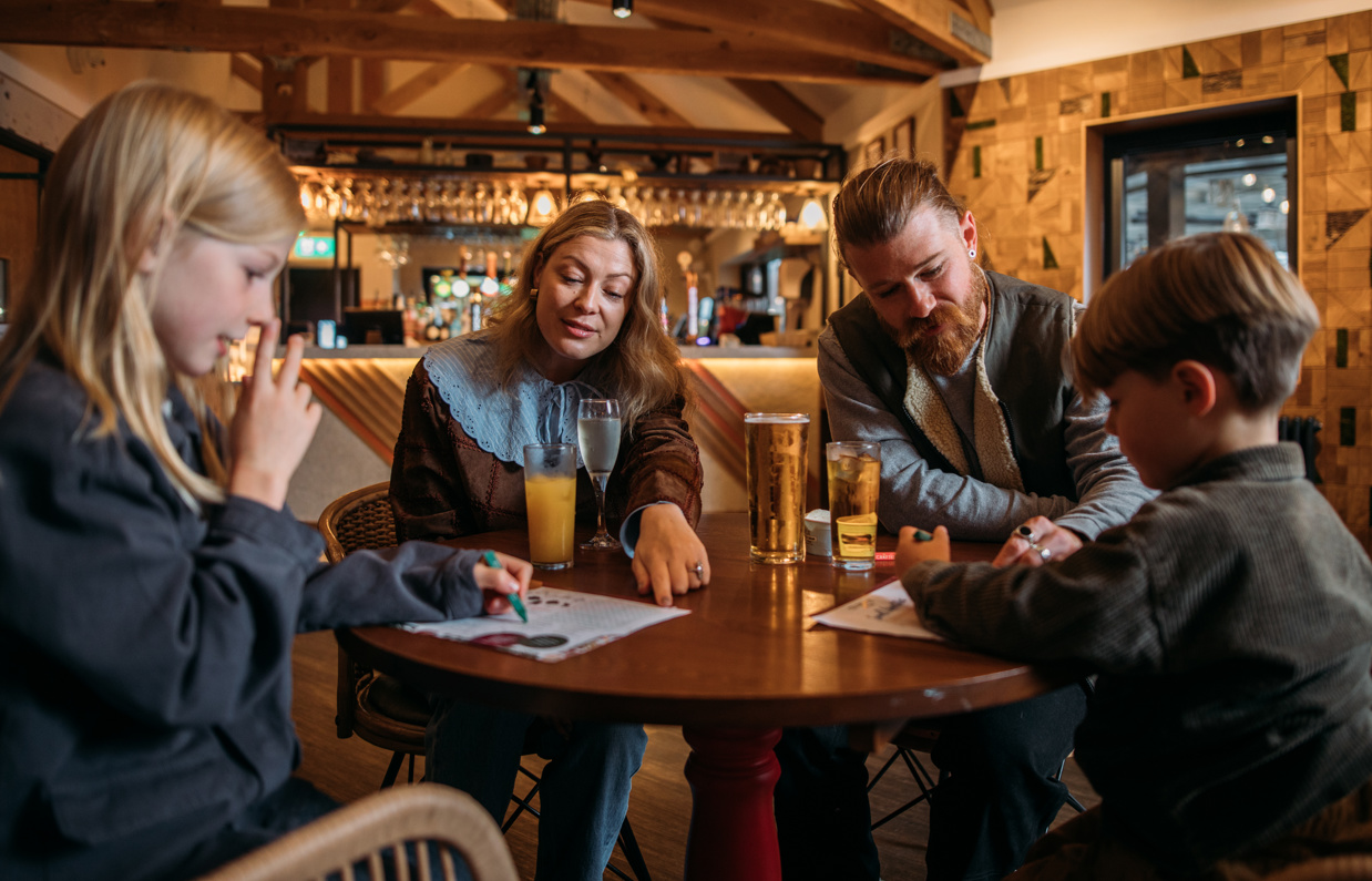 A couple sat with two young boys at an indoor table with drinks and colouring sheets