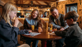 A couple sat with two young boys at an indoor table with drinks and colouring sheets
