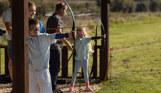 Two young children in a field with activity leaders aiming archery bows at targets