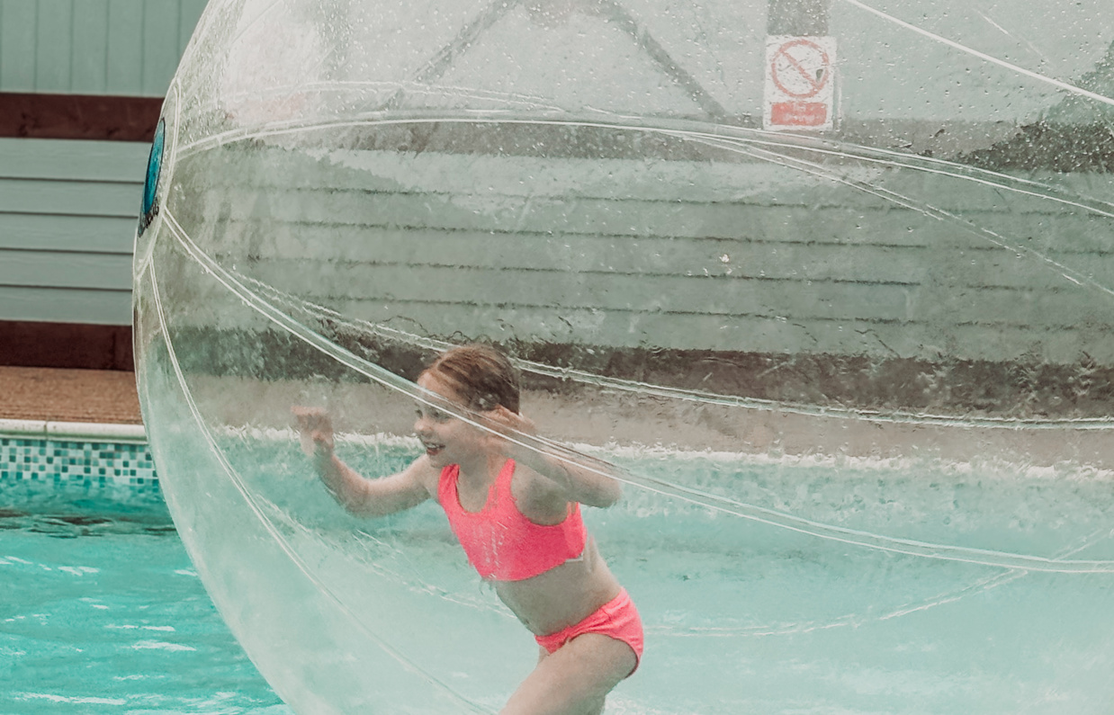 A young girl running in a water zorb ball on a swimming pool