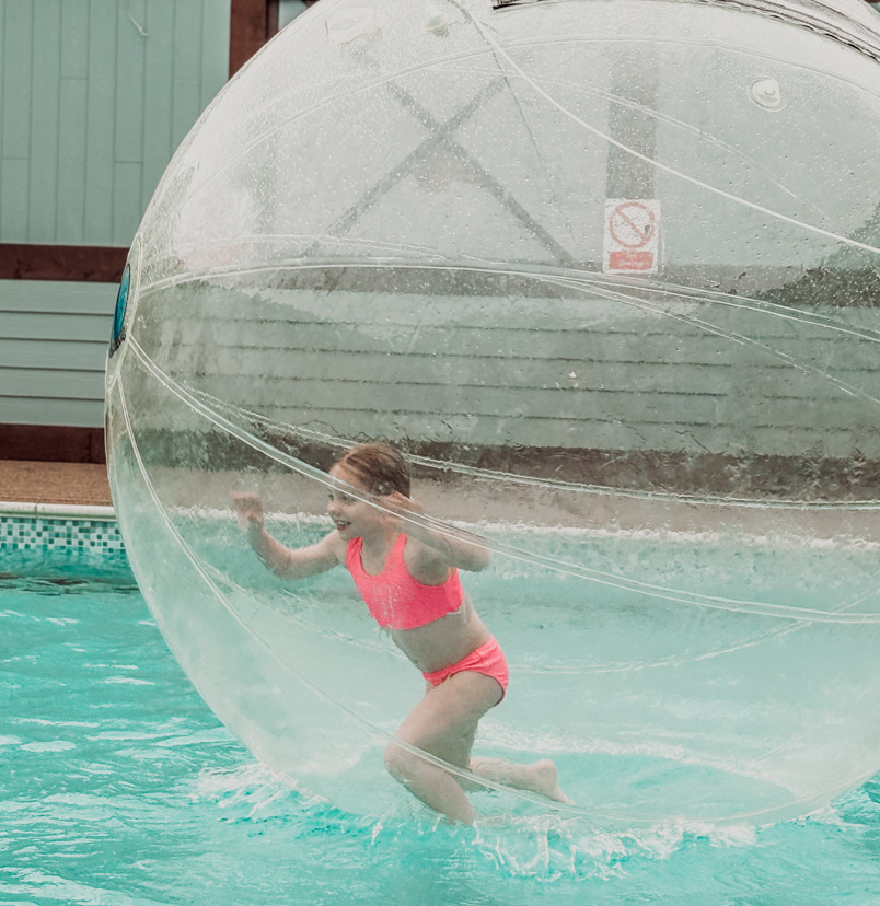 A young girl running in a water zorb ball on a swimming pool
