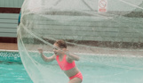 A young girl running in a water zorb ball on a swimming pool