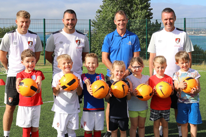A group of young children with adults all in football / sport gear holding footballs