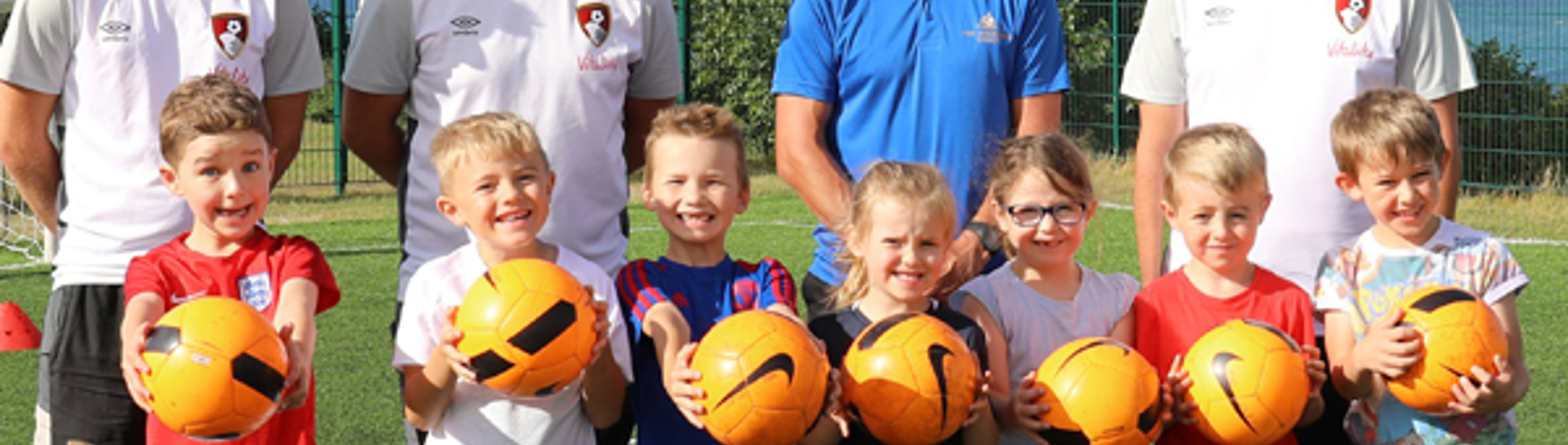 A group of young children with adults all in football / sport gear holding footballs
