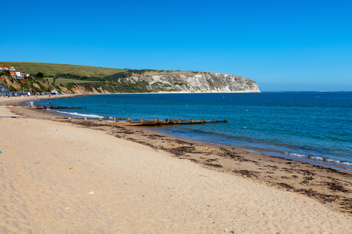 A sandy beach with blue seas and hills in the background