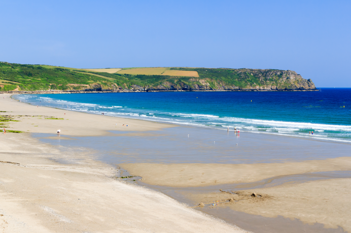 A sandy beach surrounded by blue sea and grassy headland