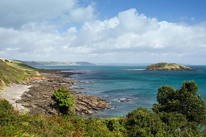 View of Looe Island from Portnader Bay with blue waters and rocky cliffsides
