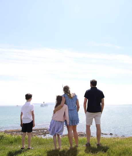 A family of four on the cliff path looking out to sea on a bright blue day with cruise ships in the distance