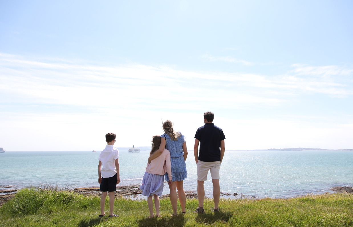 A family of four on the cliff path looking out to sea on a bright blue day with cruise ships in the distance