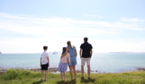 A family of four on the cliff path looking out to sea on a bright blue day with cruise ships in the distance