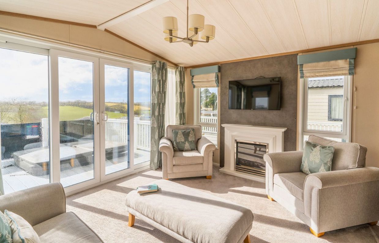 Internal of a caravan open plan living space with sliding doors onto decking with hot tub and countryside views