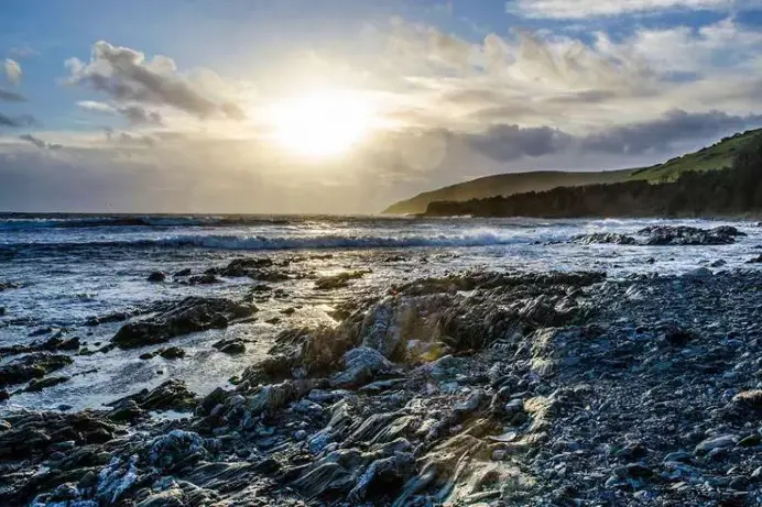 A shingle beach with waves hitting the rocks and a dramatic sunset