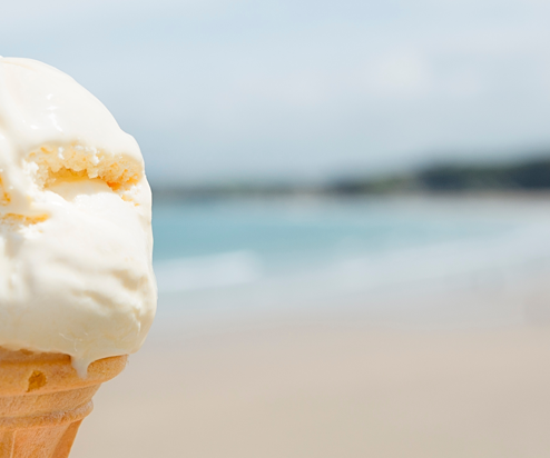 A vanilla ice cream on a cone with a chocolate flake and the backdrop of the sea