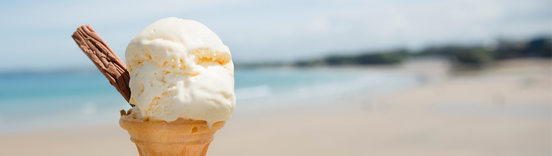 A vanilla ice cream on a cone with a chocolate flake and the backdrop of the sea
