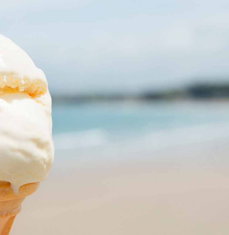 A vanilla ice cream on a cone with a chocolate flake and the backdrop of the sea