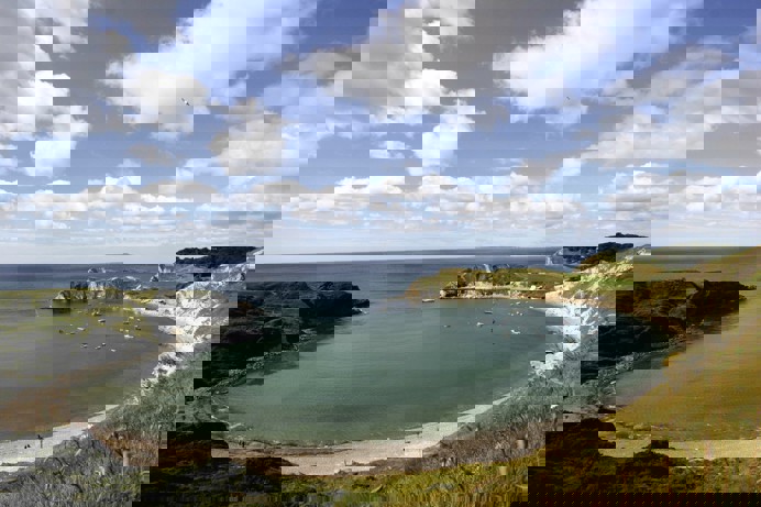 A natural horse-shoe shaped cove with boats in the sea and blue sky