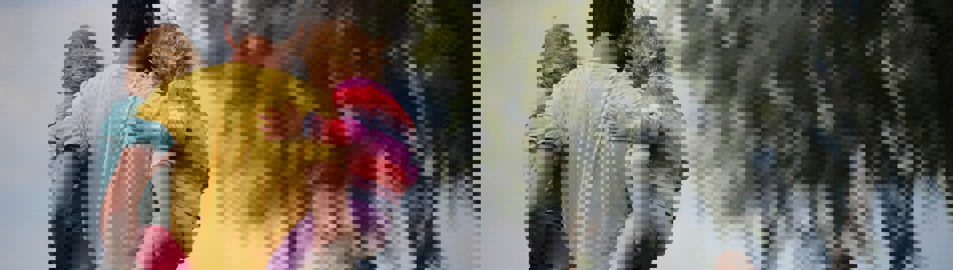 A man carrying two young girls on his hips with a young boy running in front of him in a poppy field with trees in the distance