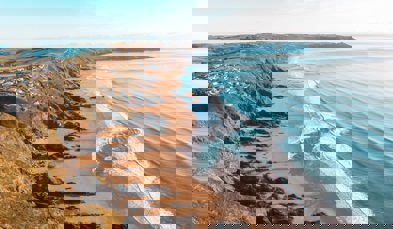 A long stretch of beach with rocky cliffside and blue waves on a sunny, blue sky day