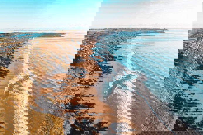 A long stretch of beach with rocky cliffside and blue waves on a sunny, blue sky day