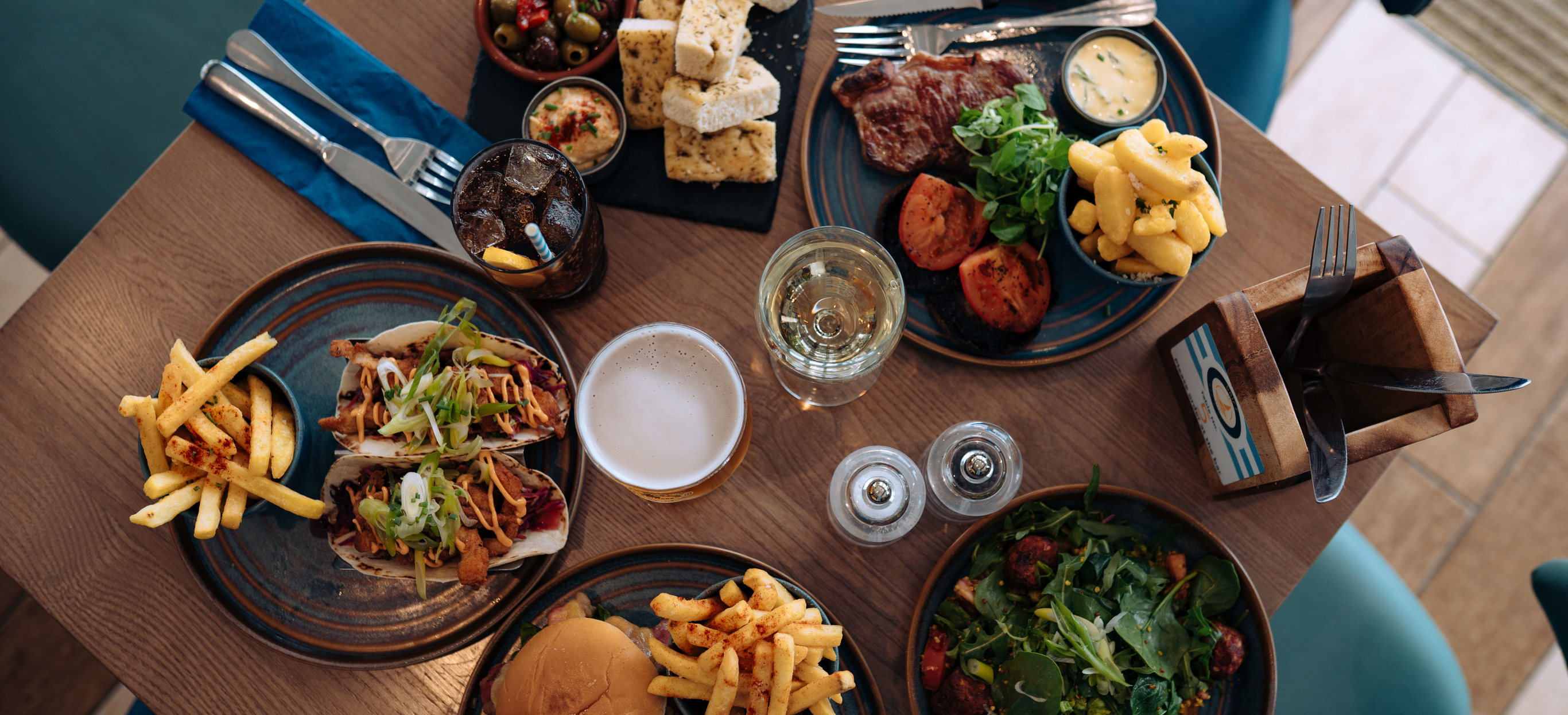 A selection of dishes including steak, burgers, tacos, salad and charcuterie board, taken from above