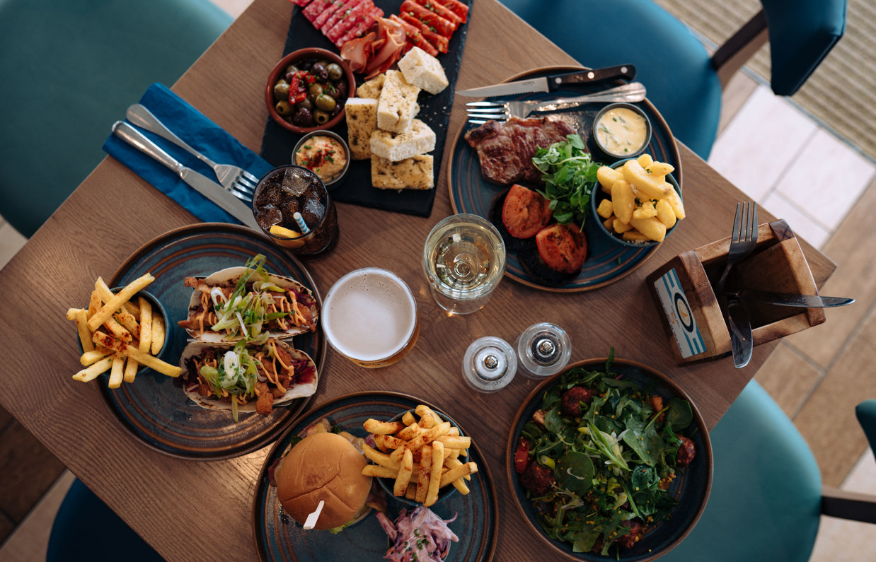 A selection of dishes including steak, burgers, tacos, salad and charcuterie board, taken from above
