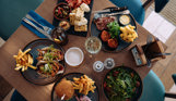 A selection of dishes including steak, burgers, tacos, salad and charcuterie board, taken from above