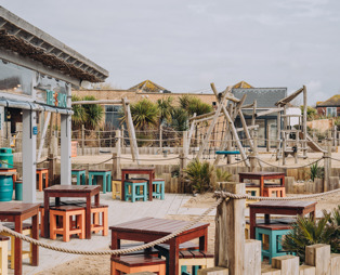 An outdoor beach bar and street food shack with outdoor seating and a children's play area by the sea