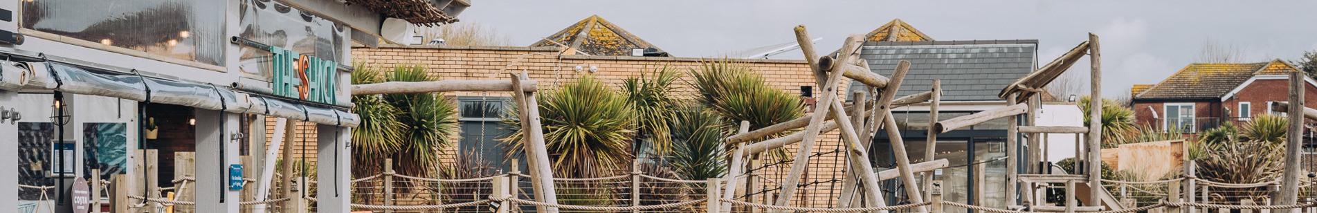 An outdoor beach bar and street food shack with outdoor seating and a children's play area by the sea