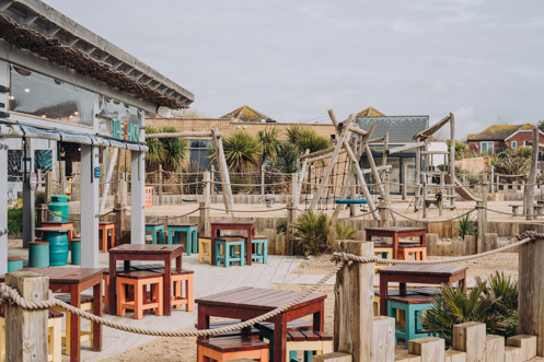 An outdoor beach bar and street food shack with outdoor seating and a children's play area by the sea