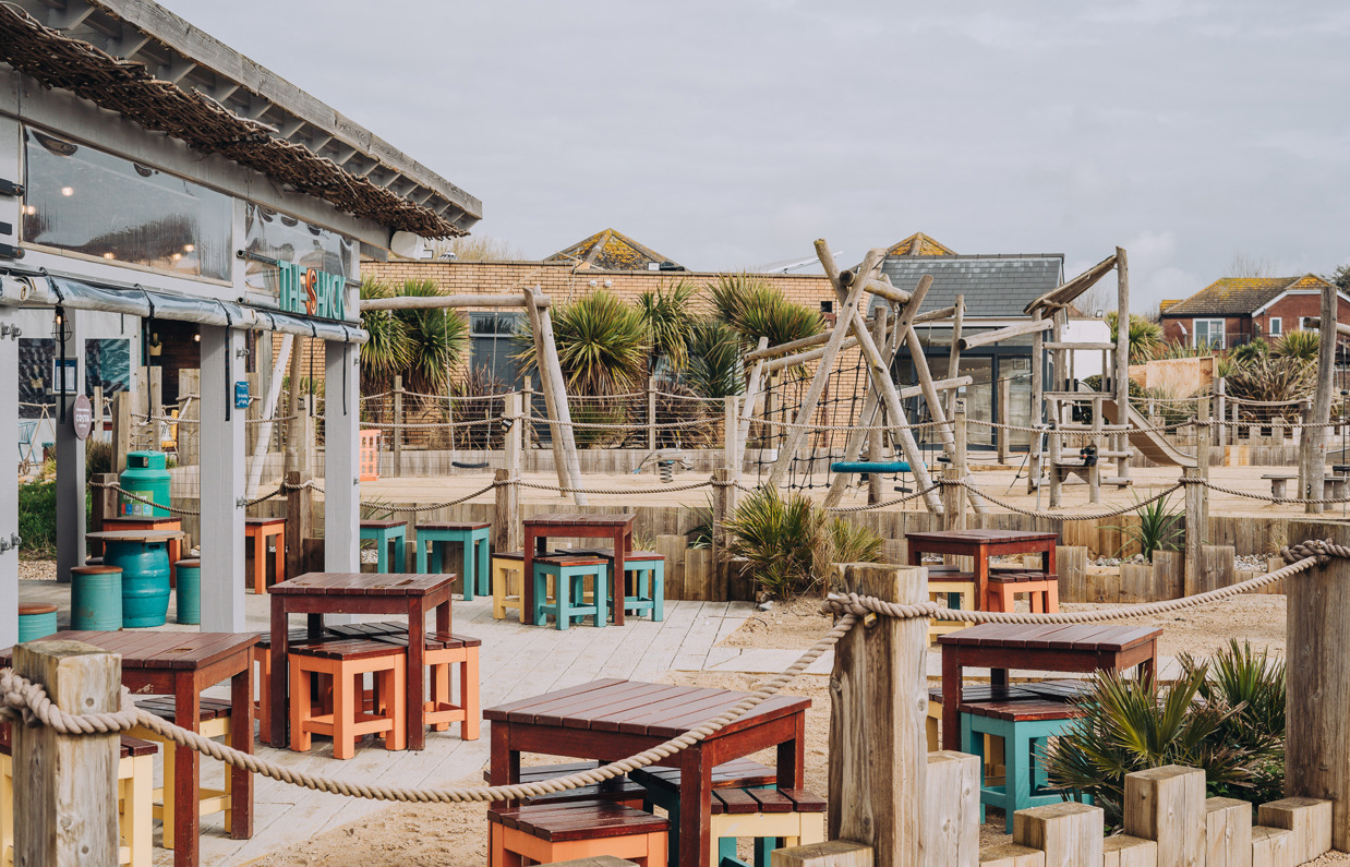 An outdoor beach bar and street food shack with outdoor seating and a children's play area by the sea