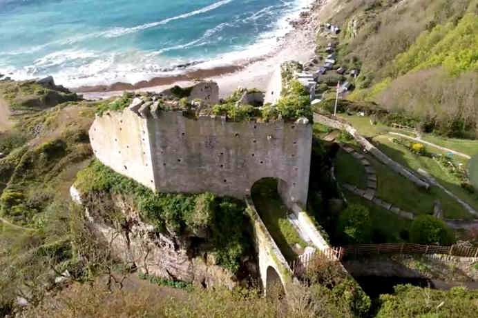 A castle remains atop a hill mound by the coast with views of the sea