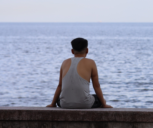 A man sat on a wall doing nothing looking out to sea