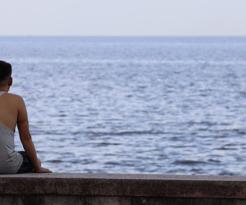 A man sat on a wall doing nothing looking out to sea