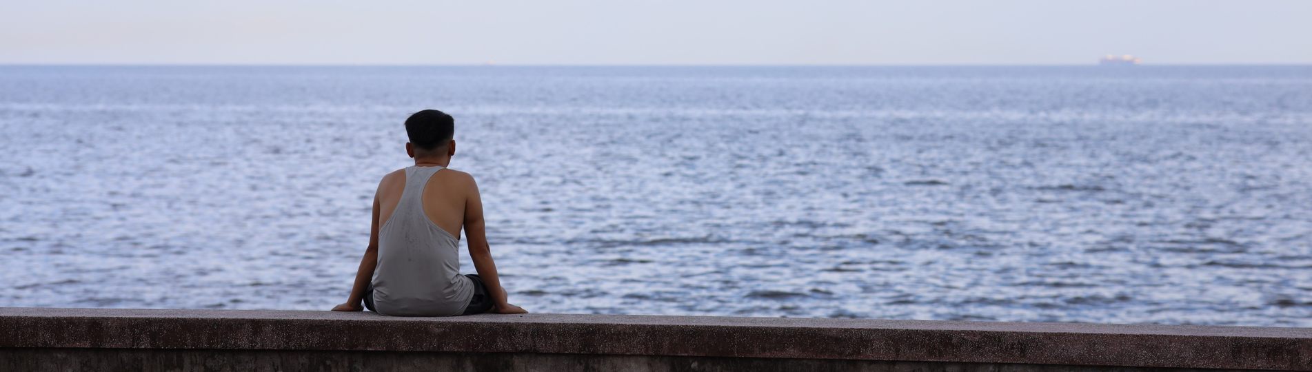 A man sat on a wall doing nothing looking out to sea