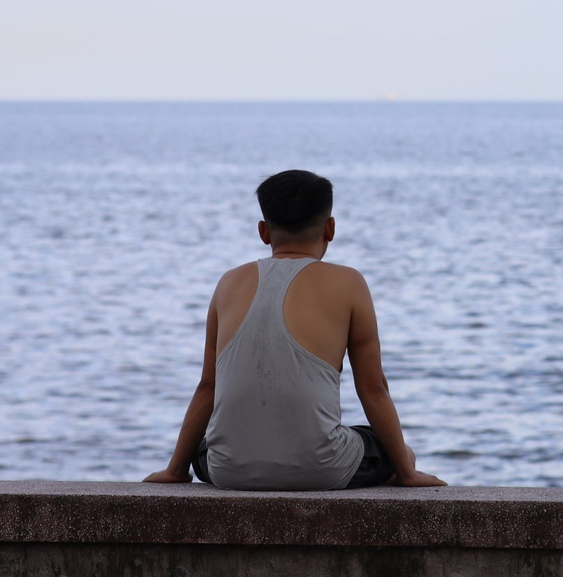 A man sat on a wall doing nothing looking out to sea