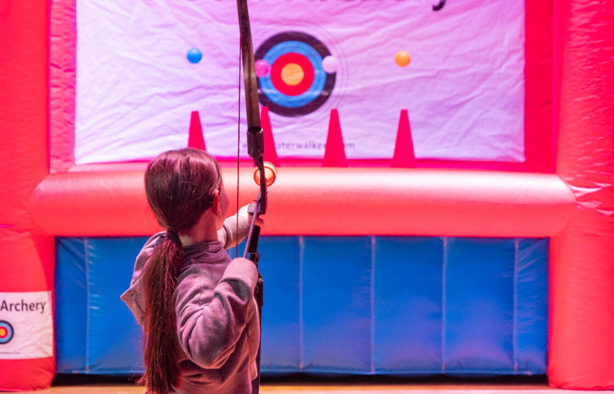 A young girl aiming a hover archery bow at the inflatable target